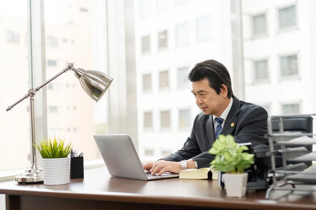 オフィスでノートパソコンに向かい、真剣な表情で仕事をする中年の日本人ビジネスマン