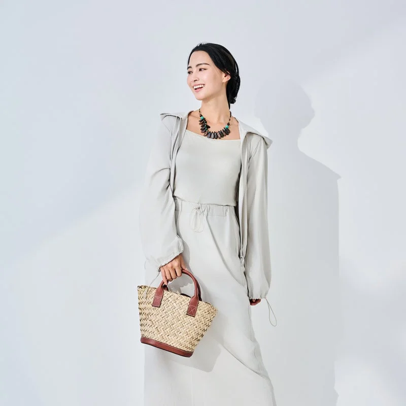 白い背景の前で、ベージュ系のワントーンコーデを着こなした女性が笑顔で立っています。