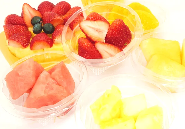 様々な種類のカットフルーツが透明な容器に盛られた様子を捉えた画像です。いちごがたっぷりのタルトを中心に、スイカやパイナップルなどが鮮やかに並べられています。