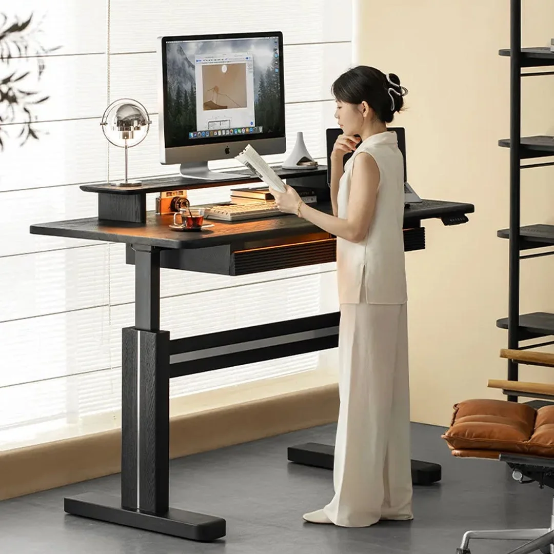 モダンなスタンディングデスクで、一人の女性が本を読みながら立っている様子。パソコンモニターも置かれ、シンプルでスタイリッシュな書斎やオフィス空間で仕事や休憩をしている場面が描かれています。