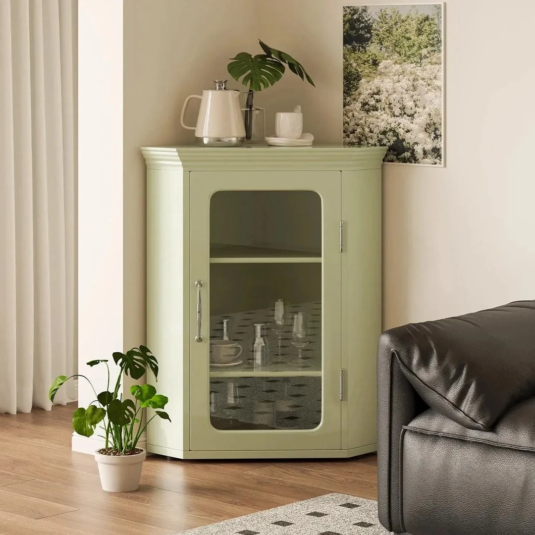 淡い緑色のコーナーキャビネットが部屋の角に置かれたリビングルームの様子です。キャビネット上部には白いティーポットとモンステラの葉が飾られ、内部にはグラスやカップが整然と並べられています。床には鉢植えのモンステラがあり、落ち着いたモダンな空間を演出しています。