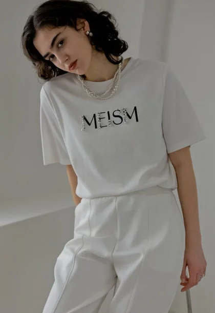 白いTシャツと白いパンツを着用し、パールネックレスを身につけた女性