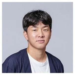 グレーの背景を背にした、黒髪の若い男性のポートレート写真