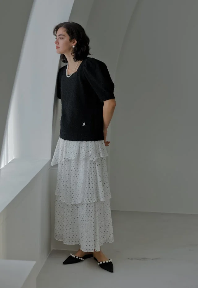 白いティアードのドット柄スカートと黒いパフスリーブのトップスを着用した女性