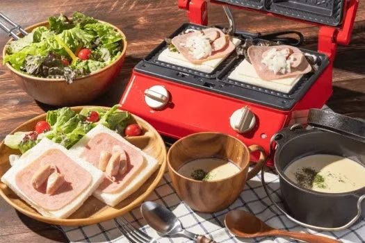 ホットサンドメーカーで調理中のホットサンドと、サラダ、ハムとソーセージのオープンサンド、スープが並んだ美味しそうな朝食