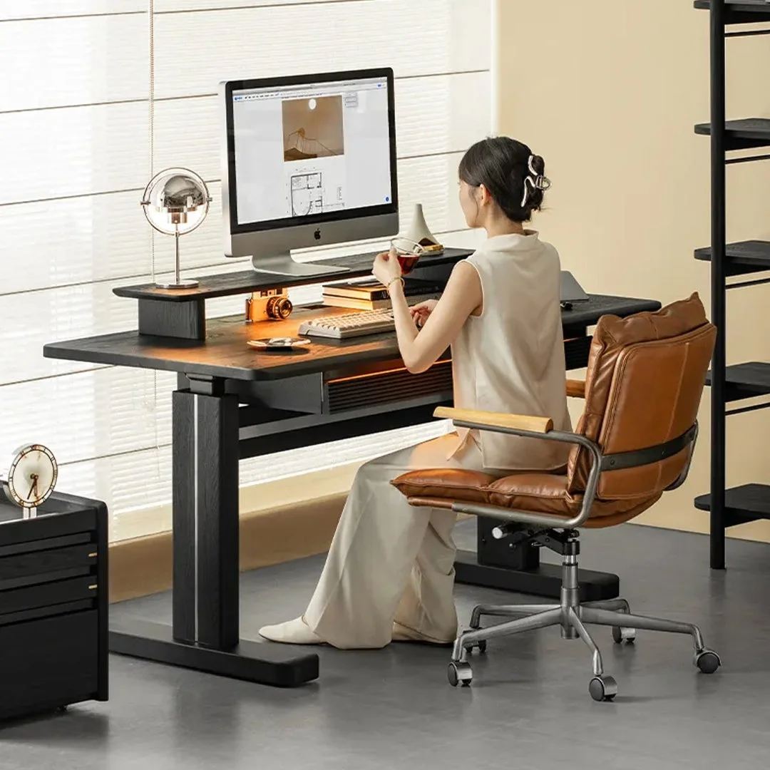 モダンなオフィス空間で、女性がApple iMacを使ってPC作業をしている様子。快適そうなブラウンの革製チェアに座り、集中して画面上のデザイン資料を見ている。スタイリッシュで機能的なワークスペースが印象的です。