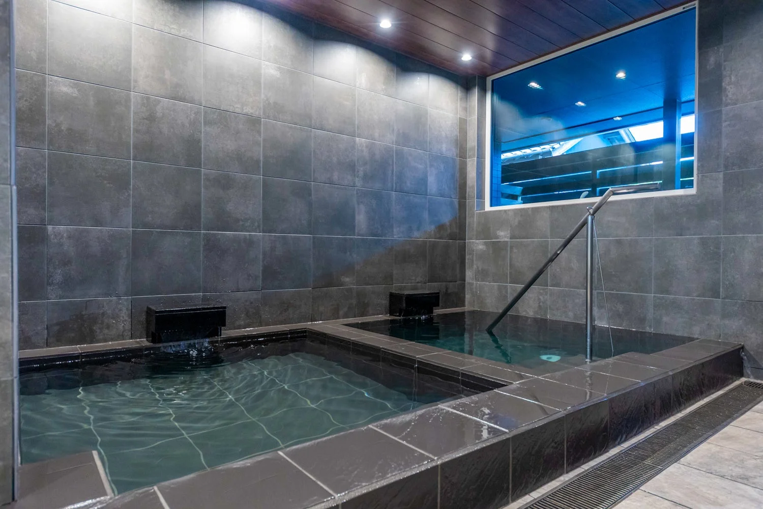 ダークグレーのタイル張りの壁と木目調の天井が特徴のモダンな内湯