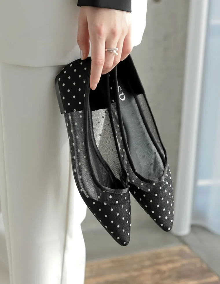 女性が黒い水玉模様のポインテッドトゥフラットシューズを手に持っている画像