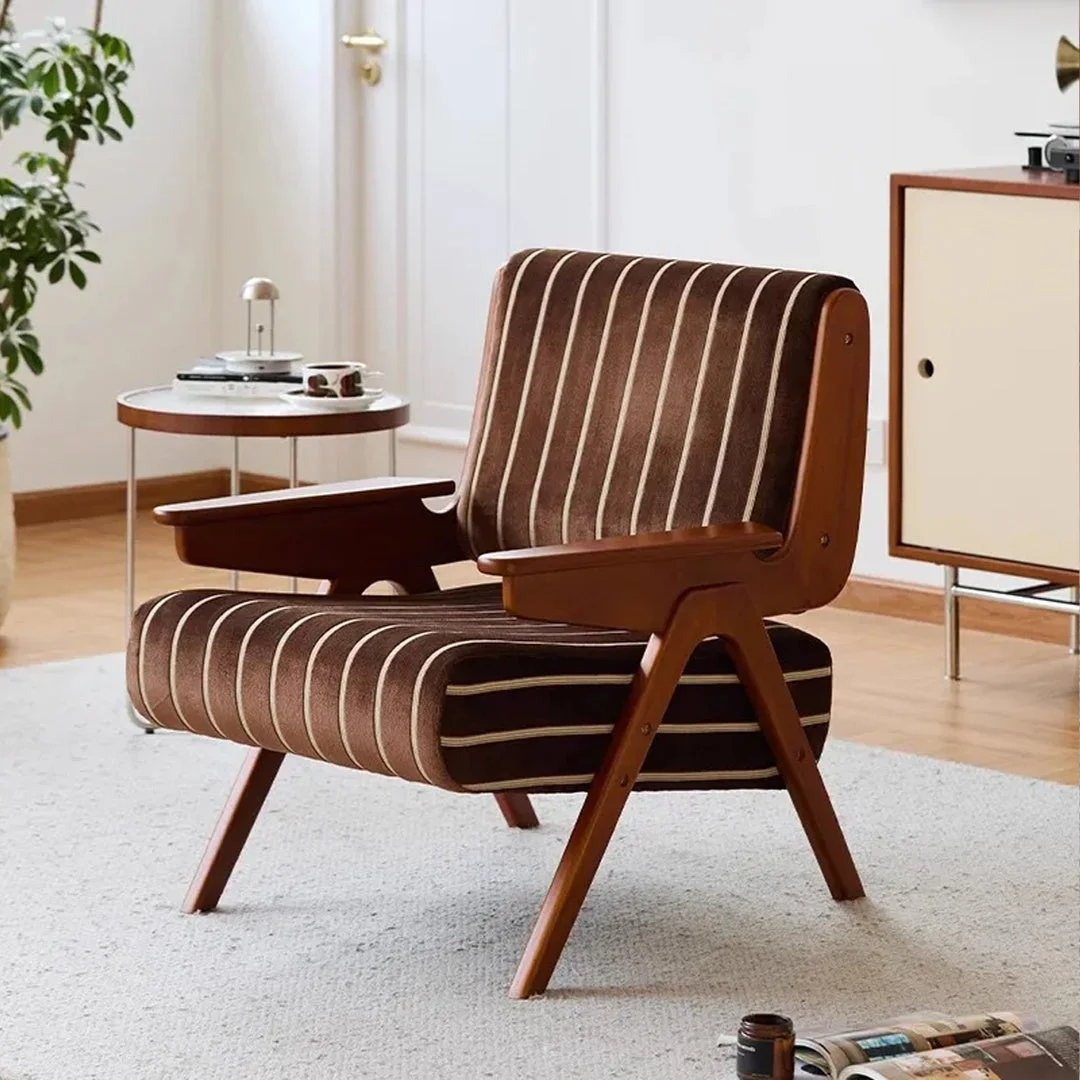 木製のアームと脚を持つ茶色のストライプ柄のアームチェアが、明るいリビングルームに置かれています。サイドテーブルにはカップと植物、キャビネットの上にはレコードプレーヤーがあり、レトロモダンな雰囲気のインテリアです。