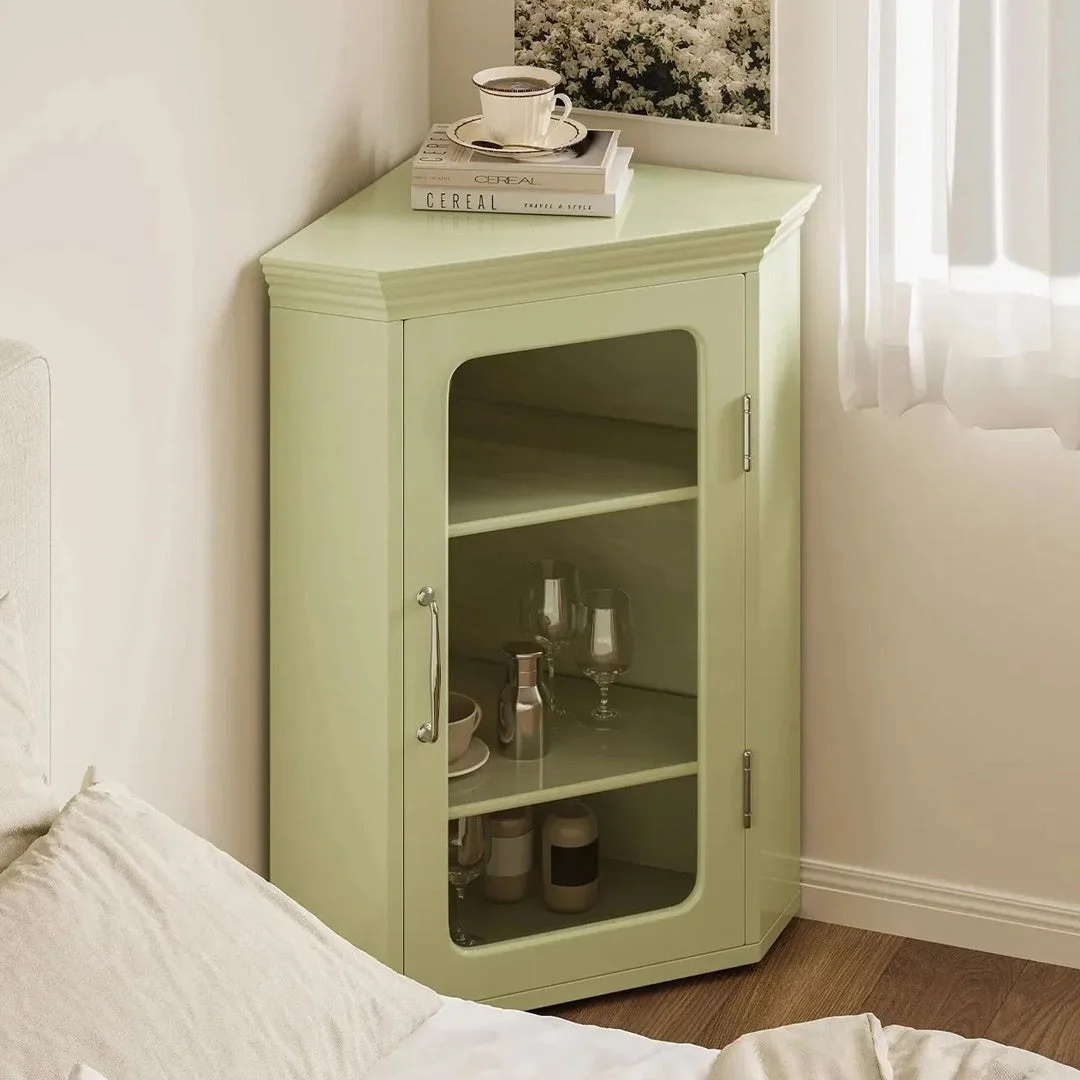 淡い緑色のコーナーキャビネットが部屋の隅に置かれ、上には本とティーカップ、中にはグラスやボトルが収納されています。窓からの光が差し込む、すっきりとした寝室のインテリアです。