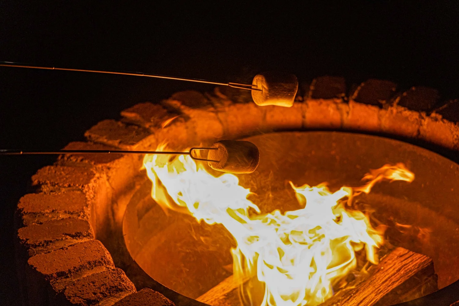 夜のファイヤーピットで、炎を囲んでマシュマロを焼いている様子