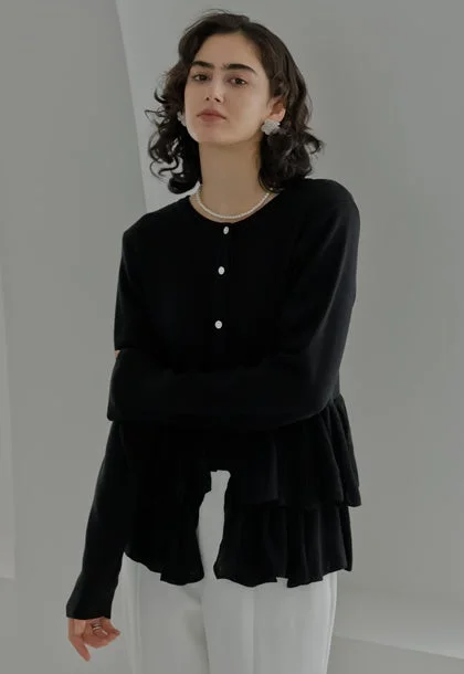 黒いティアードデザインのカーディガンと白いパンツを着用した女性