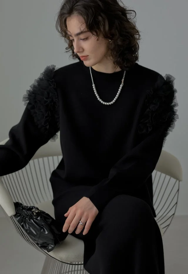 黒いフリルスリーブのトップスとパールネックレスを着用した女性