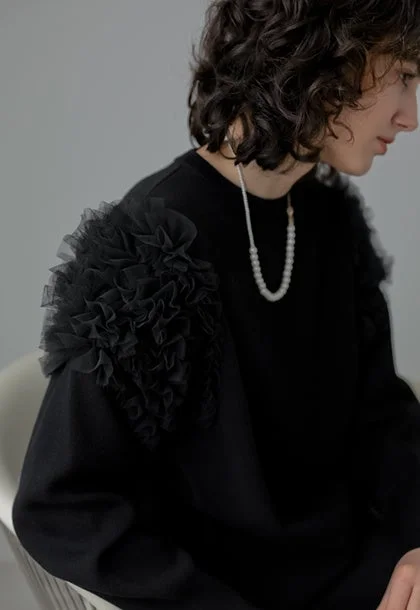 黒いフリル付きトップスを着用し、パールネックレスをつけた女性