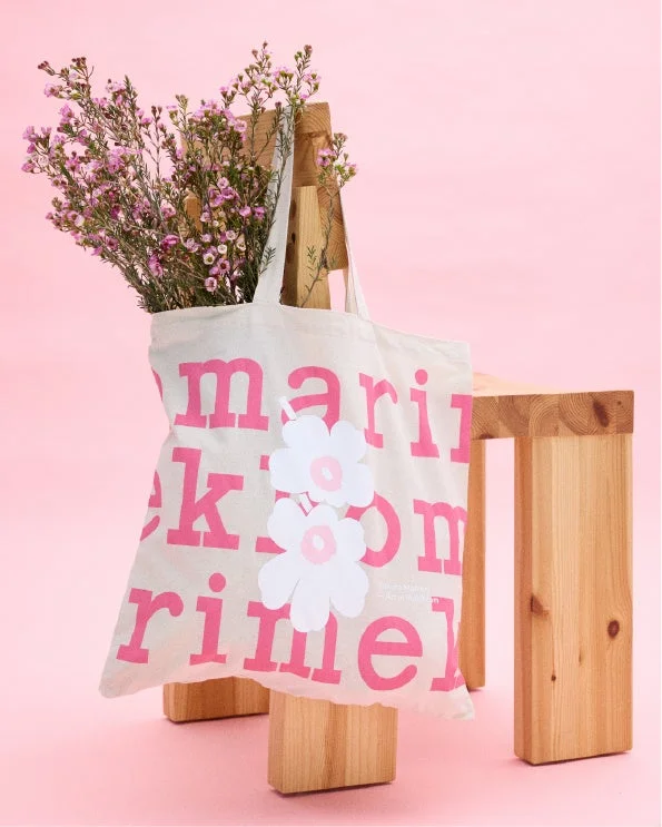 ピンクのロゴと白い花の装飾が施されたマリメッコの白いトートバッグ