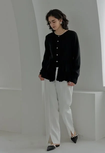 黒のペプラムカーディガンと白のスリット入りワイドパンツを着用した女性