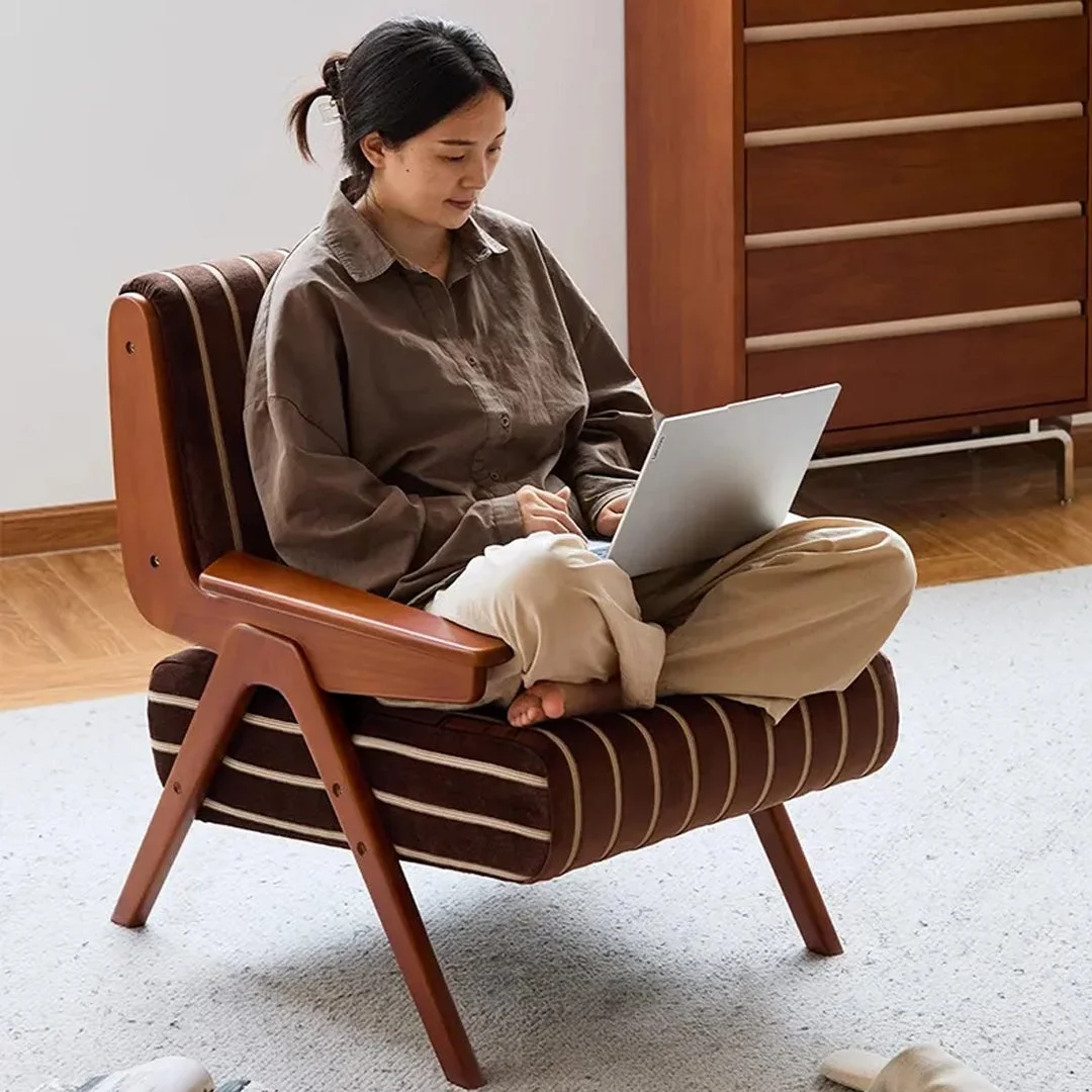 ストライプ柄のアームチェアに座り、ノートパソコンを操作する女性の様子。自宅でくつろぎながら作業に集中している様子がうかがえ、落ち着いた雰囲気のインテリアが特徴的です。