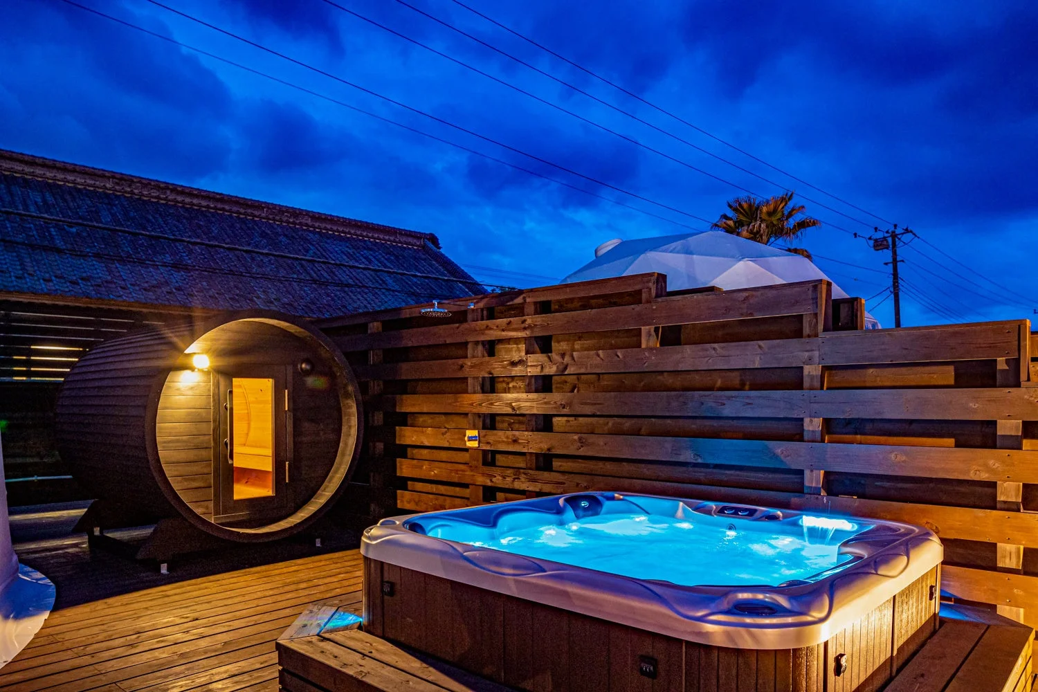 夜の屋外に設置されたバレルサウナと、青く光るジャグジー