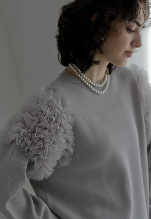 フリル袖が特徴的なライトグレーのセーターを着用し、二連のパールネックレスを合わせた女性
