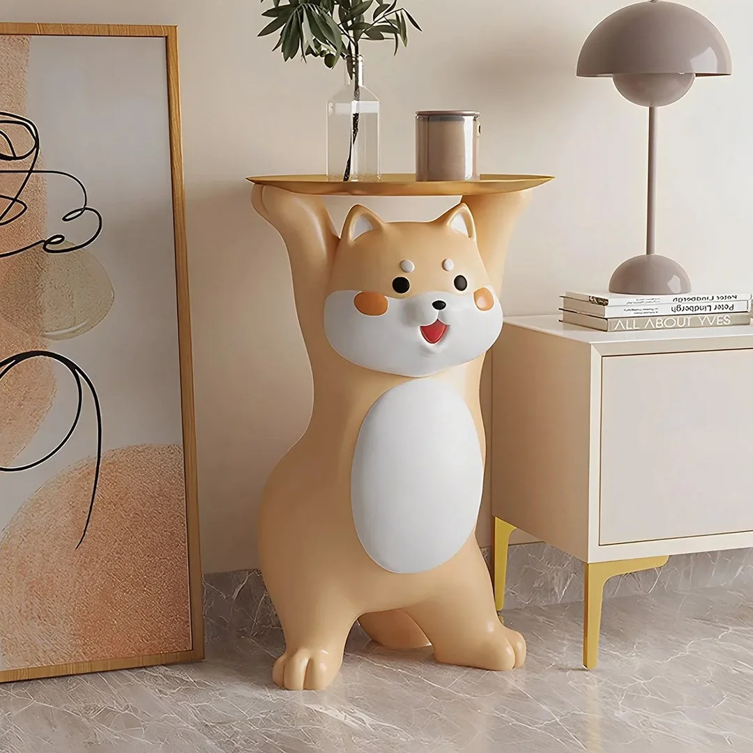 可愛らしい柴犬のような犬のキャラクターが、頭上にトレイを掲げた置物です。トレイには花瓶が置かれ、隣にはモダンなサイドテーブル、ランプ、本、抽象画が見えます。リビングを彩るユニークで魅力的なインテリアです。