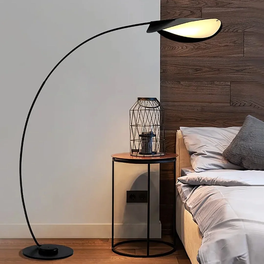 モダンな寝室の一角で、黒いアーチ状のフロアランプが柔らかな光を放っています。ベッドの横には木目調の天板と黒いフレームのサイドテーブルがあり、個性的なワイヤーケージの装飾品が置かれ、洗練された空間を演出しています。