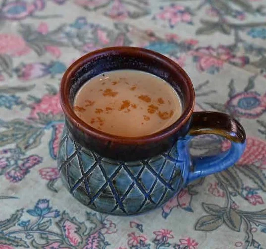 花柄のテーブルクロスの上に置かれたチャイのマグカップ