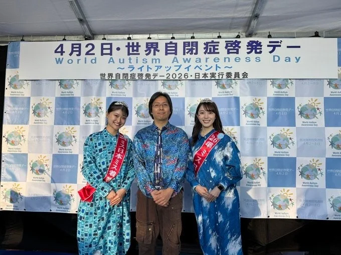 世界自閉症啓発デーのイベントで記念撮影するミス日本の方々と司会者