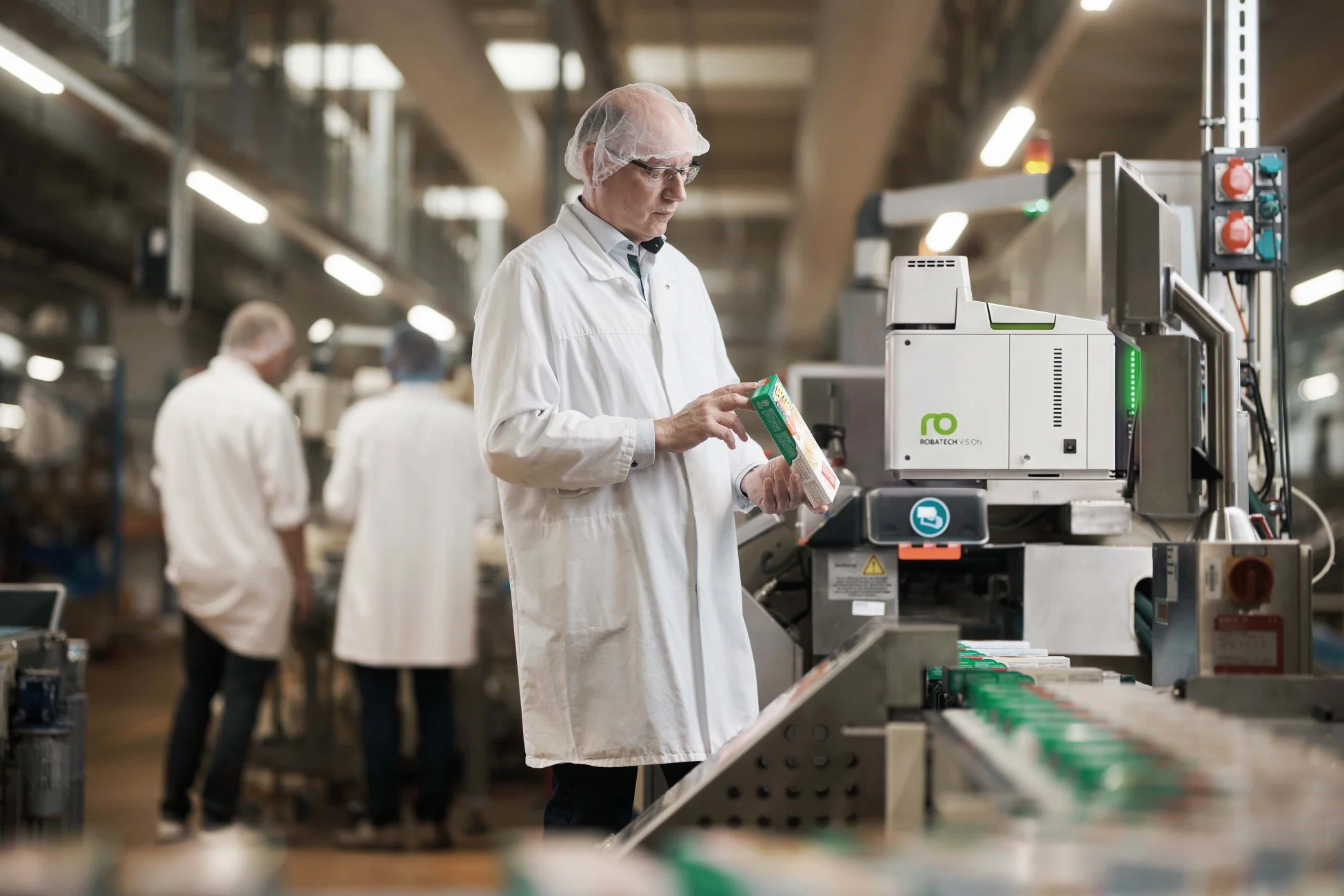 白衣を着た作業員が工場内の生産ラインで製品パッケージを検査している。