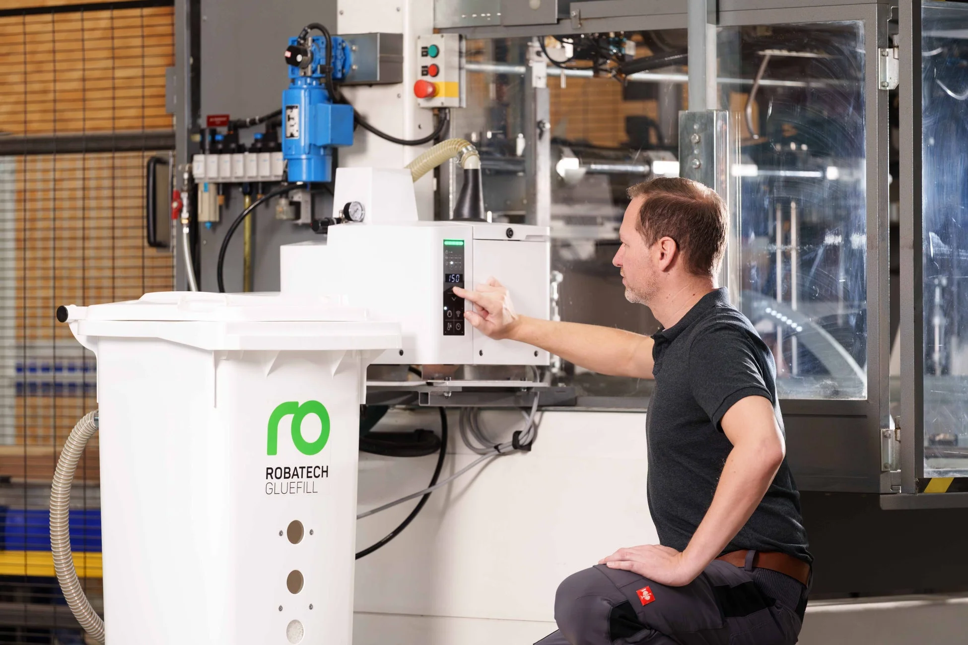 男性が産業機械「ROBATECH GLUEFILL」の操作パネルを調整している様子。