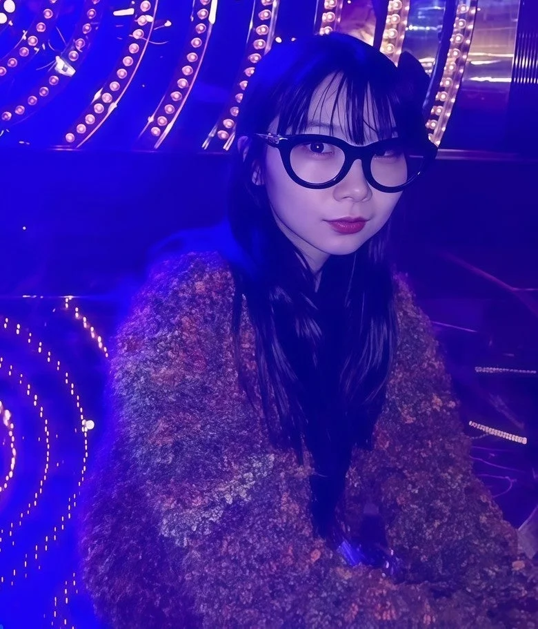 青い照明が印象的な空間で、メガネをかけた女性がカメラを見つめているポートレート。