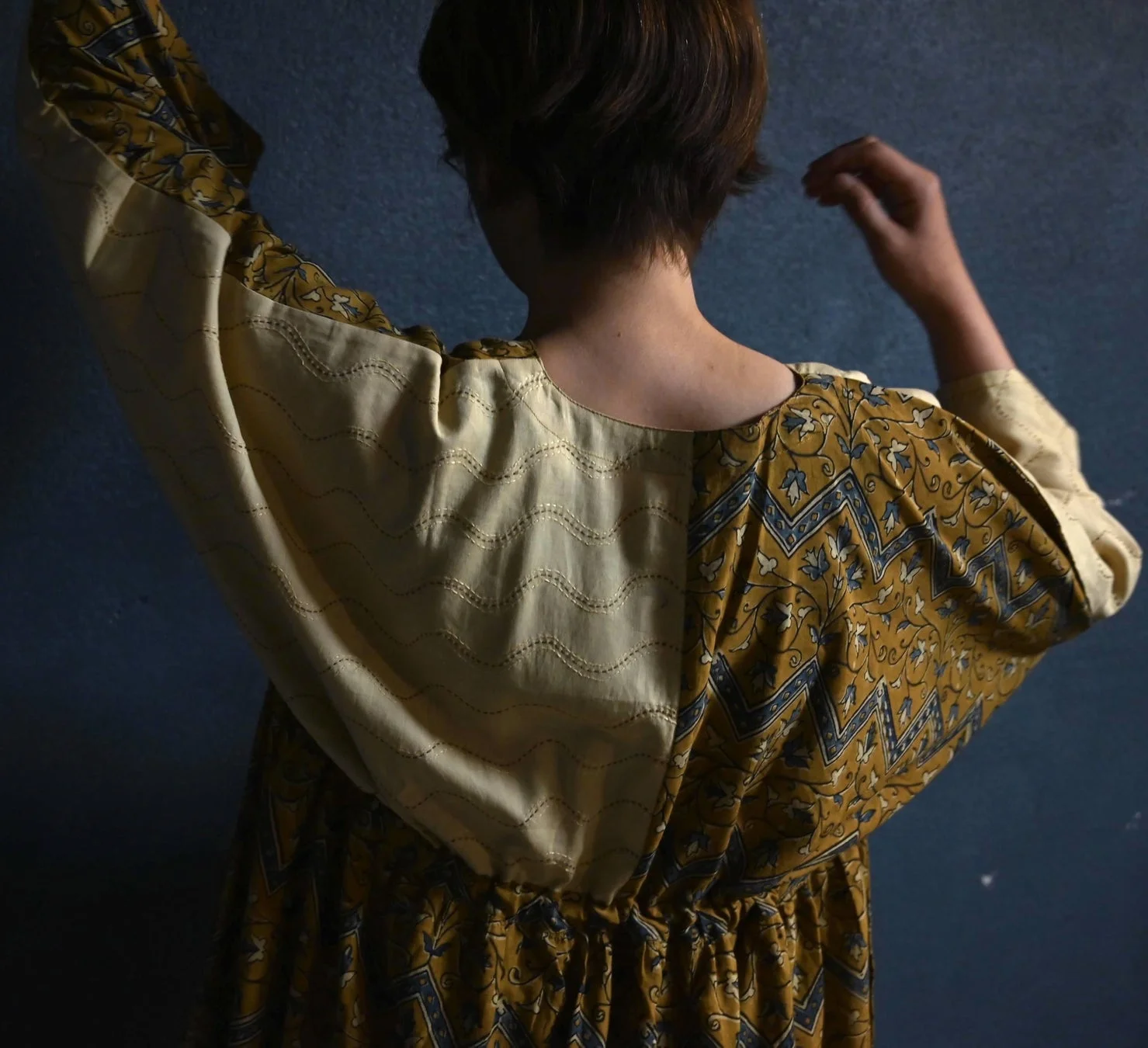 マスタードイエローとブルーのエスニック柄のワンピースを着た女性の後ろ姿