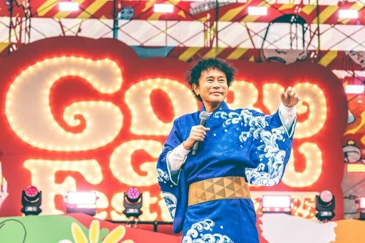 伝統的な青い和装を着てマイクを持つ男性