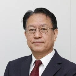 眼鏡をかけた中年のアジア人男性が、ダークスーツと赤いネクタイを着用し、正面を向いているポートレート写真
