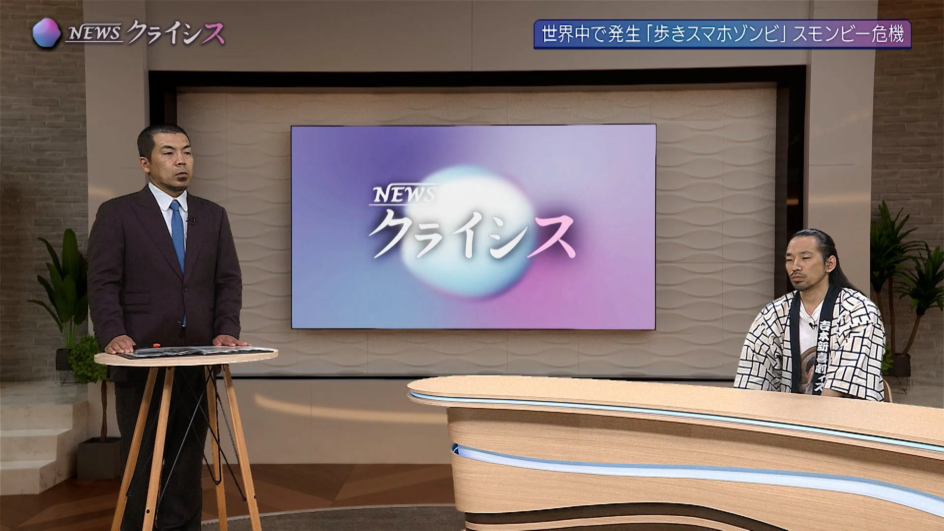 「NEWS クライシス」という番組のスタジオで、スーツ姿の男性と和装の男性が座るニュース番組の様子。画面には「歩きスマホゾンビ」スモンビー危機というテロップが表示されている。