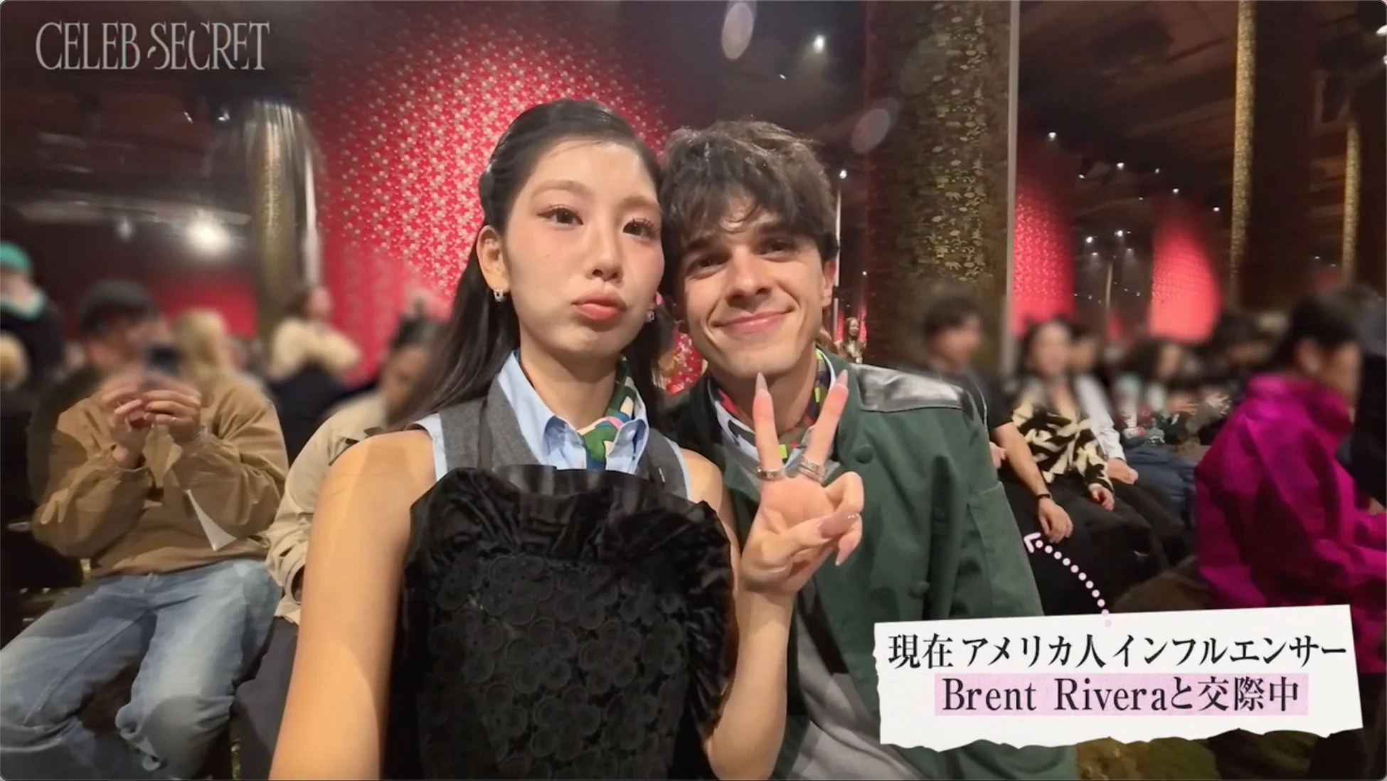 イベント会場のような場所で、日本人女性とアメリカ人インフルエンサーのBrent Riveraがセルフィーを撮っています。女性は口をすぼめて、男性は笑顔でピースサインをしており、二人が交際中であることが示されています。