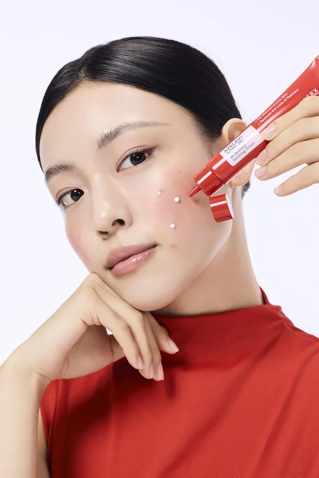 赤いチューブのスキンケアクリームを顔の赤みやニキビ跡に塗布している女性