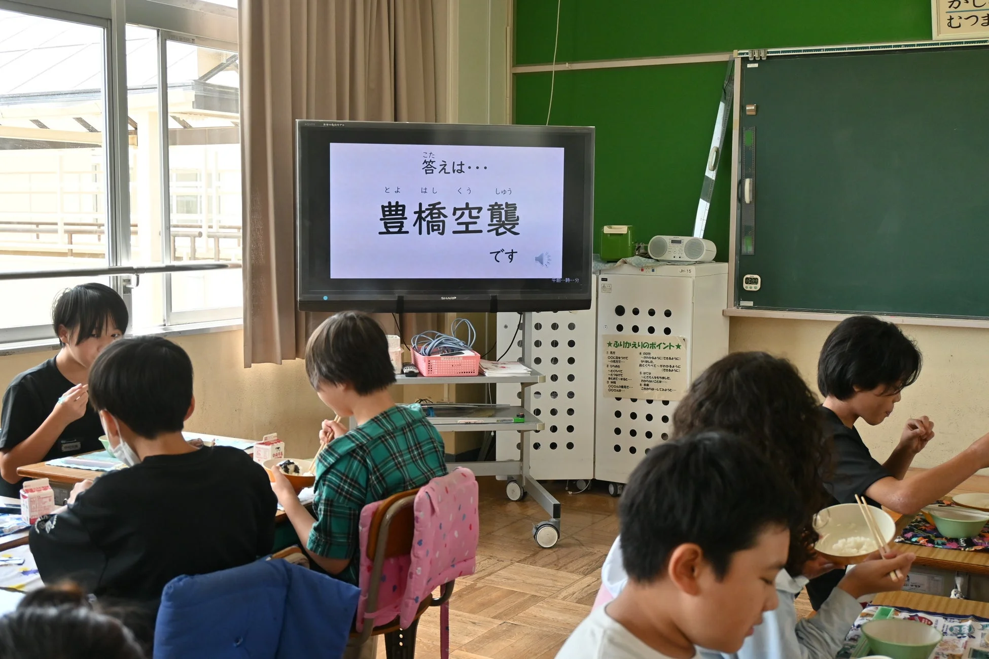給食を食べる児童たちと豊橋空襲に関するモニター