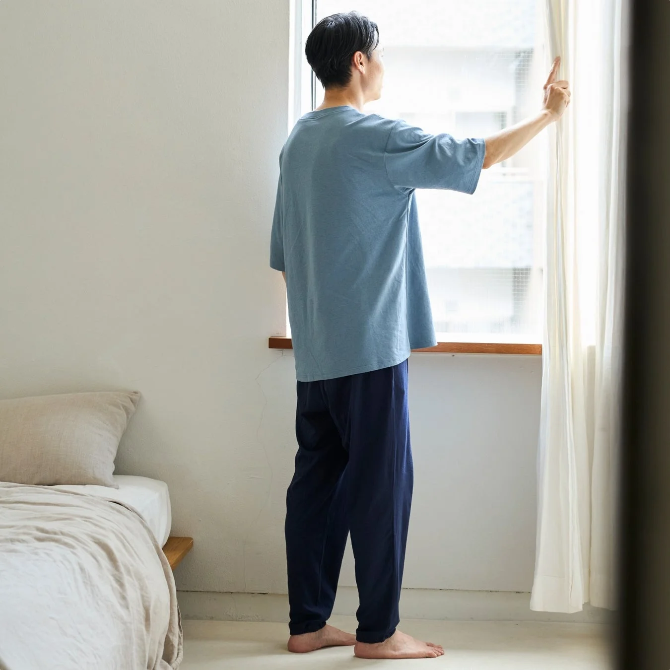 男性が部屋で窓の外を見つめる様子