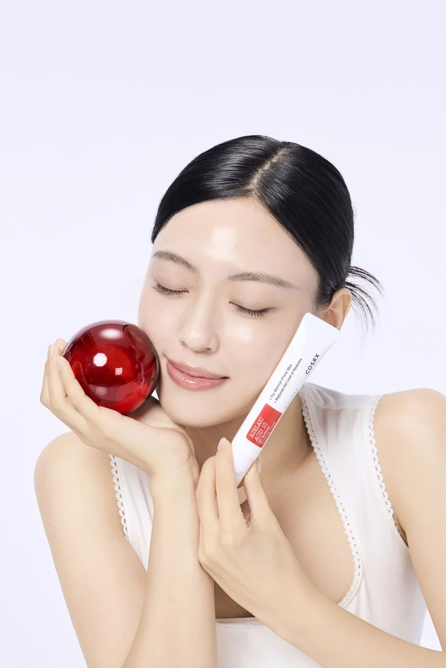 COSRXのスキンケアクリームと赤い球体を持つ女性