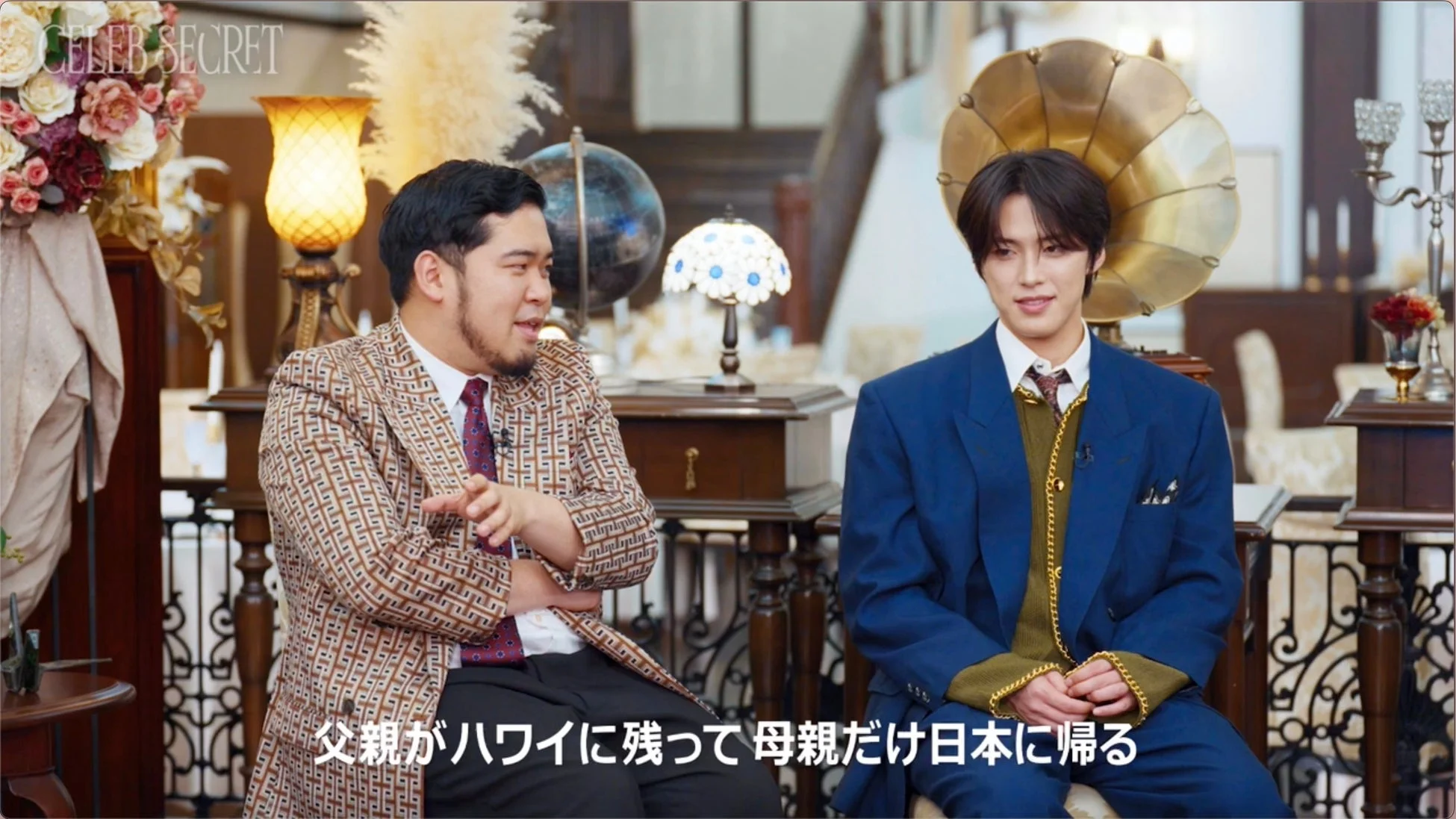 豪華な装飾の部屋で二人の男性が向かい合って座り、会話している様子。テレビ番組かインタビューの収録風景と見られ、画面下には字幕が表示されています。